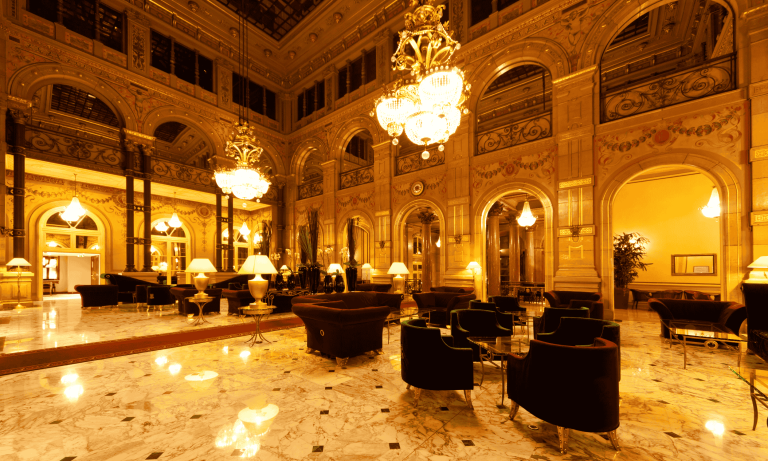 Opulent hotel lobby with marble floors, velvet armchairs, crystal chandeliers, and AI‑driven smart lighting, showcasing AI in Hospitality–powered guest personalization.